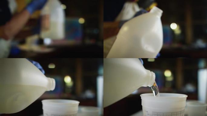 一个戴着安全手套的人将透明的环氧树脂/树脂倒入室内艺术工作室的塑料量杯中