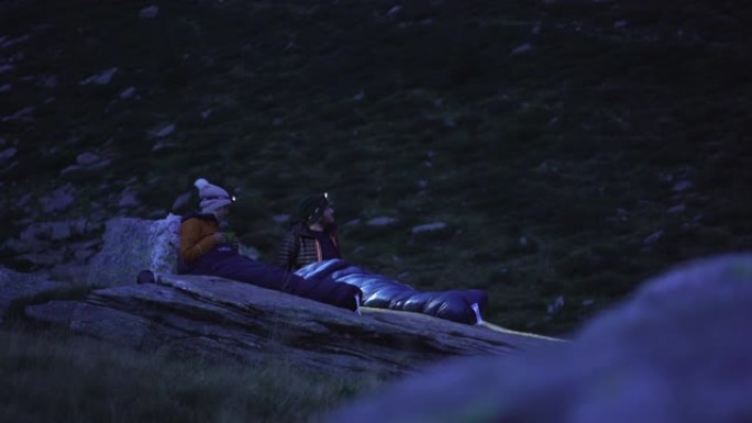 情侣比维 (bivy) 在星空下的岩石上的睡袋中露营