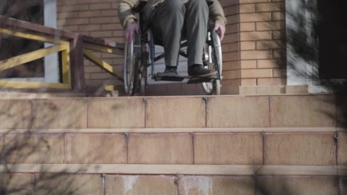 无法辨认的白人老人坐在轮椅上，滚到楼梯上停下来。残疾人没有机会滚落。坡道可用性，残疾问题。