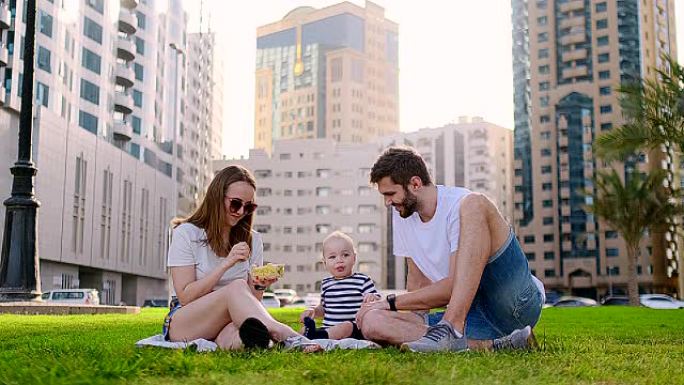 一家人坐在城市的草地上，带着一个小孩笑着。