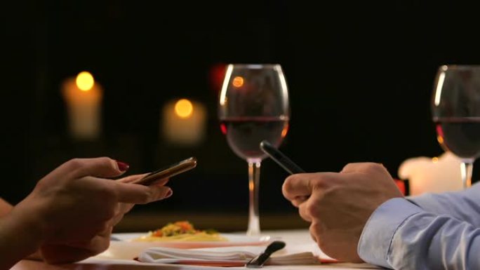 夫妇坐在餐厅里滚动智能手机，忽略了真实的交流