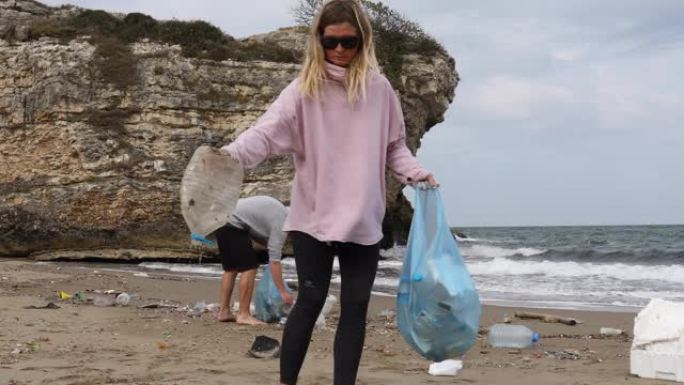 年轻的男人和女人在乱扔垃圾的海滩上收集垃圾