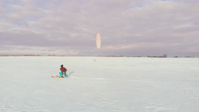 日落时，一个人在雪地里滑雪。他的降落伞拉了。风筝在雪地里冲浪