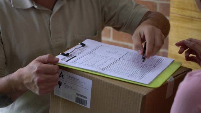 无法辨认的邮政工作人员在签单时在家中向妇女运送箱子