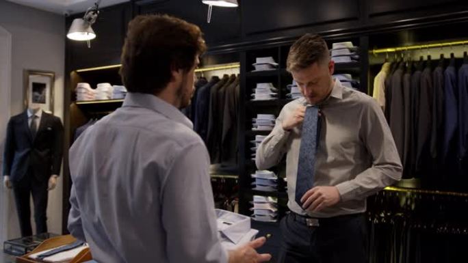 友好的推销员建议在男士商店向男性顾客穿纽扣衬衫和领带
