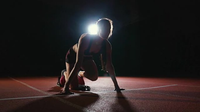 职业女运动员在黑暗的背景下，在体育场的跑道上，在黑暗的背景下，穿着运动鞋跑慢跑鞋的冲刺。平均计划
