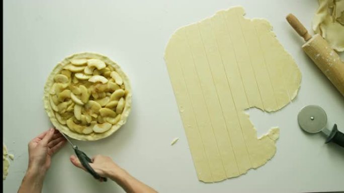 直接用厨房剪刀 (剪刀) 从装满的苹果派上切掉多余的糕点面团，旁边是切成薄片的糕点面团，a面杖和糕点