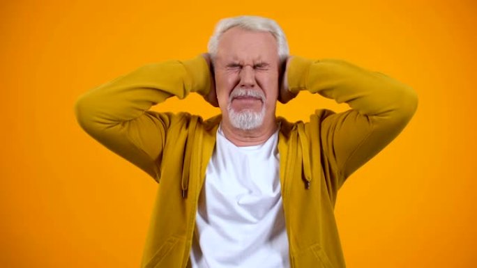 退休的男性用手掌遮住耳朵，对橙色背景上的八卦不满意