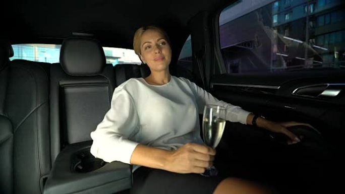疲倦的女人在汽车后座上喝香槟，与私人司机一起开车回家