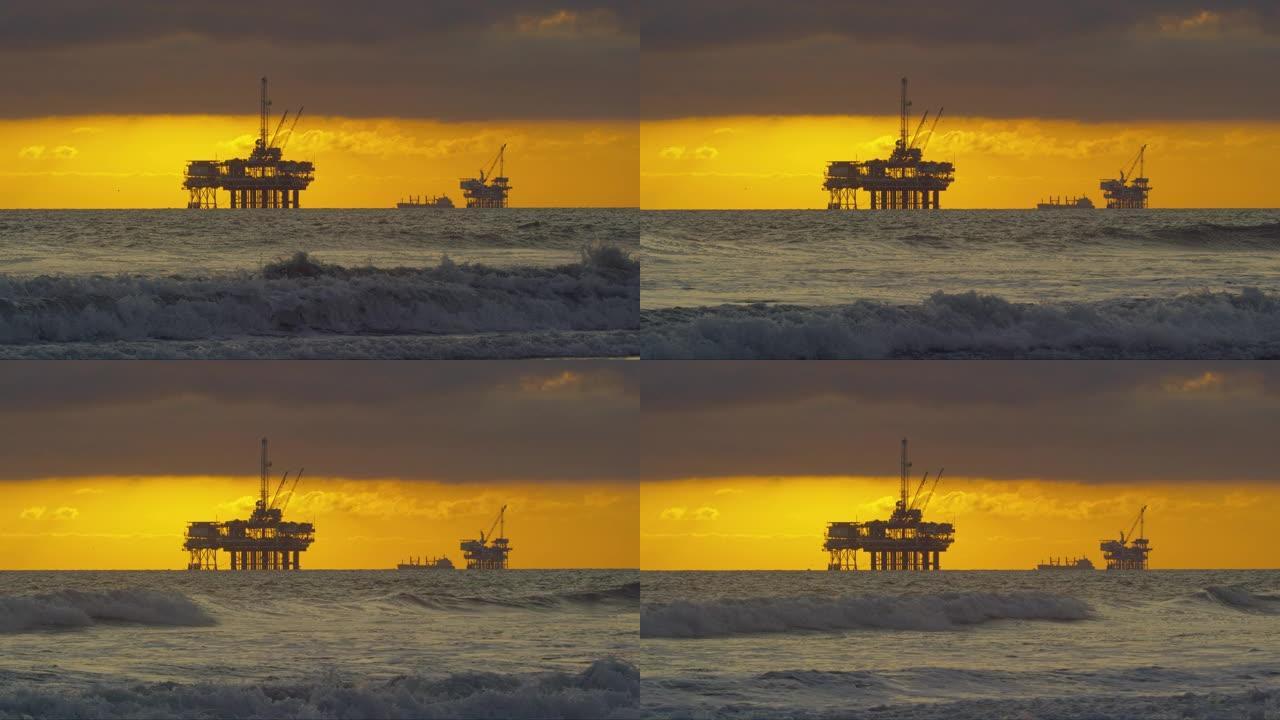 慢动作拍摄的海浪撞击到南加州的亨廷顿海滩海岸，在日落时分，远处地平线上有几个海上石油钻机平台和一艘石