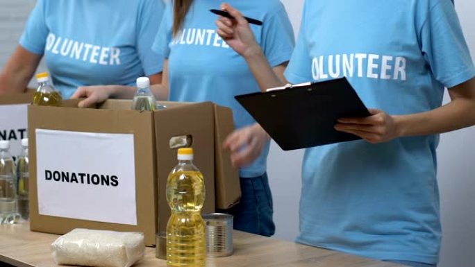 志愿者将杂货放在盒子里，而主管检查清单，捐款