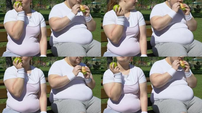 快乐的胖女孩锻炼后吃苹果，嘲笑汉堡的肥胖男人