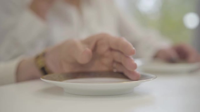 成年女性高加索人的特写镜头将杯子与茶或咖啡一起放回到盘子上。女人在咖啡馆或家里享受热饮。