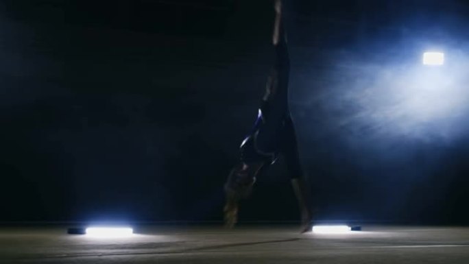 一个女孩在烟雾中的黑暗背景上表演跳跃体操