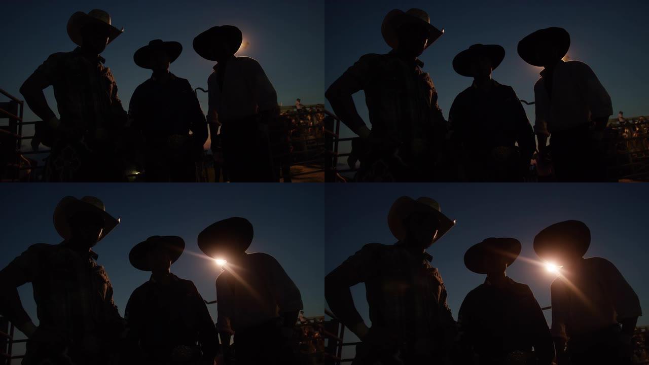 在夜间的竞争性公牛骑行活动中，三名戴着牛仔帽的剪影男子被枪杀