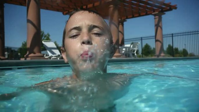 游泳池里的小男孩对着镜头吐水