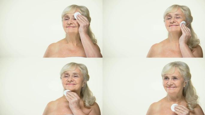 快乐的老年妇女用护垫清洁皮肤，美容护理程序，化妆品
