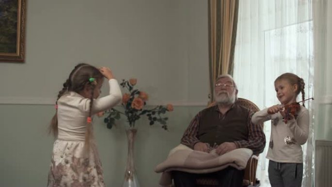 大胡子的老人坐在大窗户附近的摇椅上，看着他跳舞的孙女。