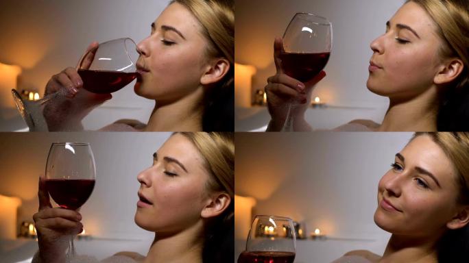 放松的女人躺在香薰蜡烛的浴缸里，享受红酒的味道，休息