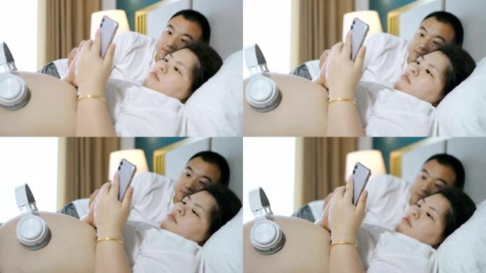 怀孕的夫妇通过耳机为未出生的婴儿播放音乐