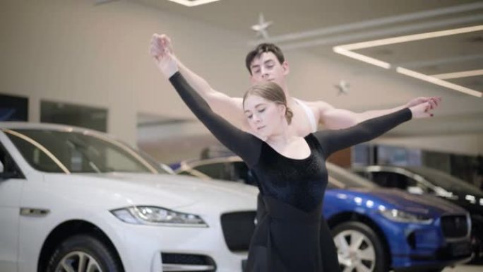 镜头跟随年轻的高加索芭蕾舞演员在汽车经销店跳舞。英俊的男人和美丽的女人在陈列室表演经典舞蹈。艺术，优