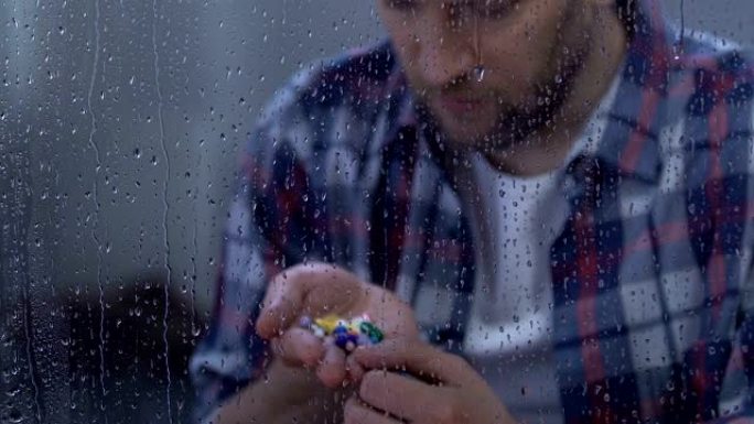 沮丧的病人拿着药，坐在下雨的窗户后面