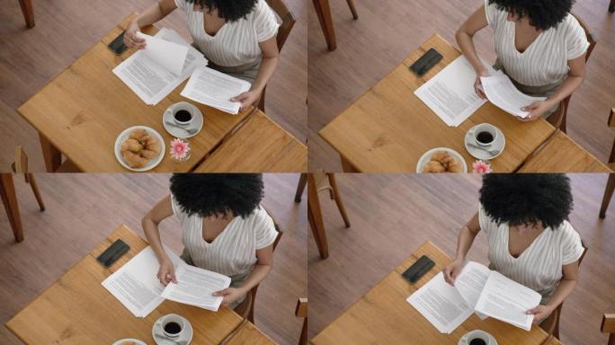 黑人女商人在咖啡店喝咖啡和吃羊角面包时检查一些文件