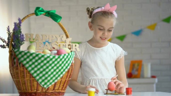 穿着白色连衣裙的创意女孩展示彩绘复活节彩蛋，装饰篮子桌