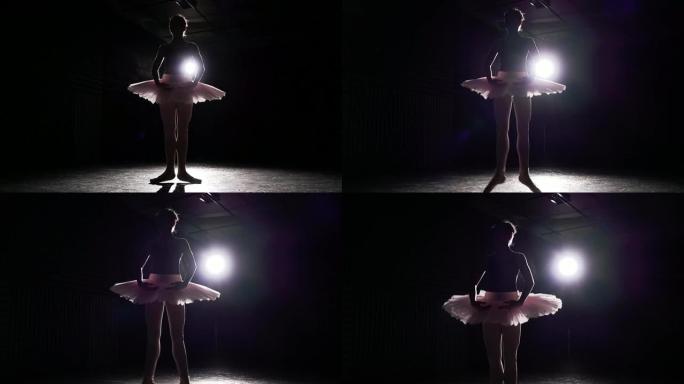 肖像专业芭蕾舞演员站在工作室黑色背景上的聚光灯下。芭蕾舞演员展示经典芭蕾舞剧。慢动作。