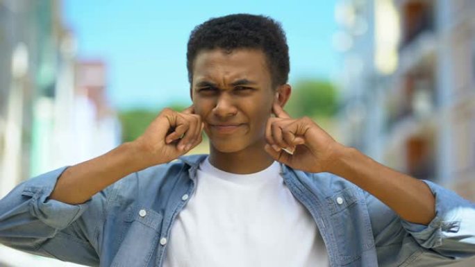 美国黑人青少年遭受巨大的街道噪音，用手指合拢耳朵