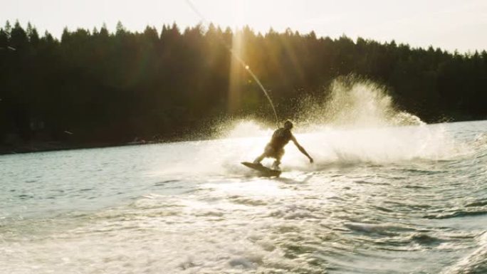 在一个阳光明媚的下午，一名二十多岁的白人男性在蒙大拿州维克多附近的格伦湖的滑水板上跳跃并表演技巧