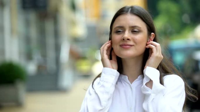美女在城市大街上戴着无线耳机，享受音乐