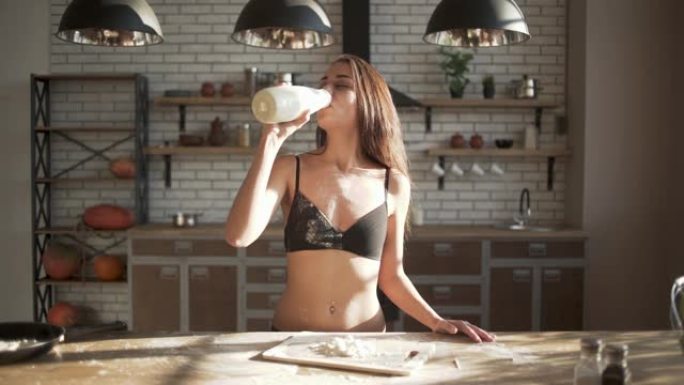 美丽的女孩喝牛奶时不小心洒了一身。早上在厨房里穿着性感内衣的幸福女人。缓慢的运动。