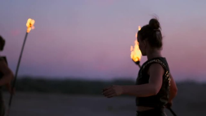 日落时分，在沙滩上放火的妇女跳舞，并以慢动作向美丽的天空展示技巧。