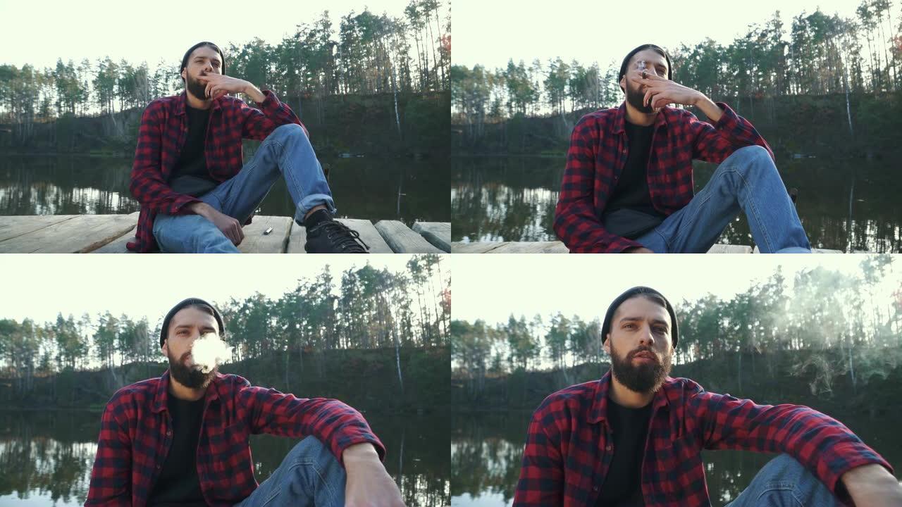 大胡子的容男坐在神奇的湖附近，抽雪茄
