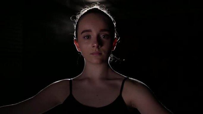 肖像专业年轻芭蕾舞演员站在工作室黑色背景上的聚光灯下。芭蕾舞演员展示经典芭蕾舞剧。慢动作。
