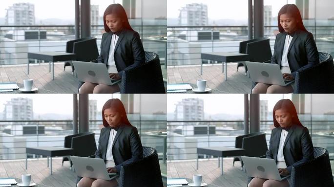 亚洲女商人坐在露台休息室俯瞰城市，在笔记本电脑上工作