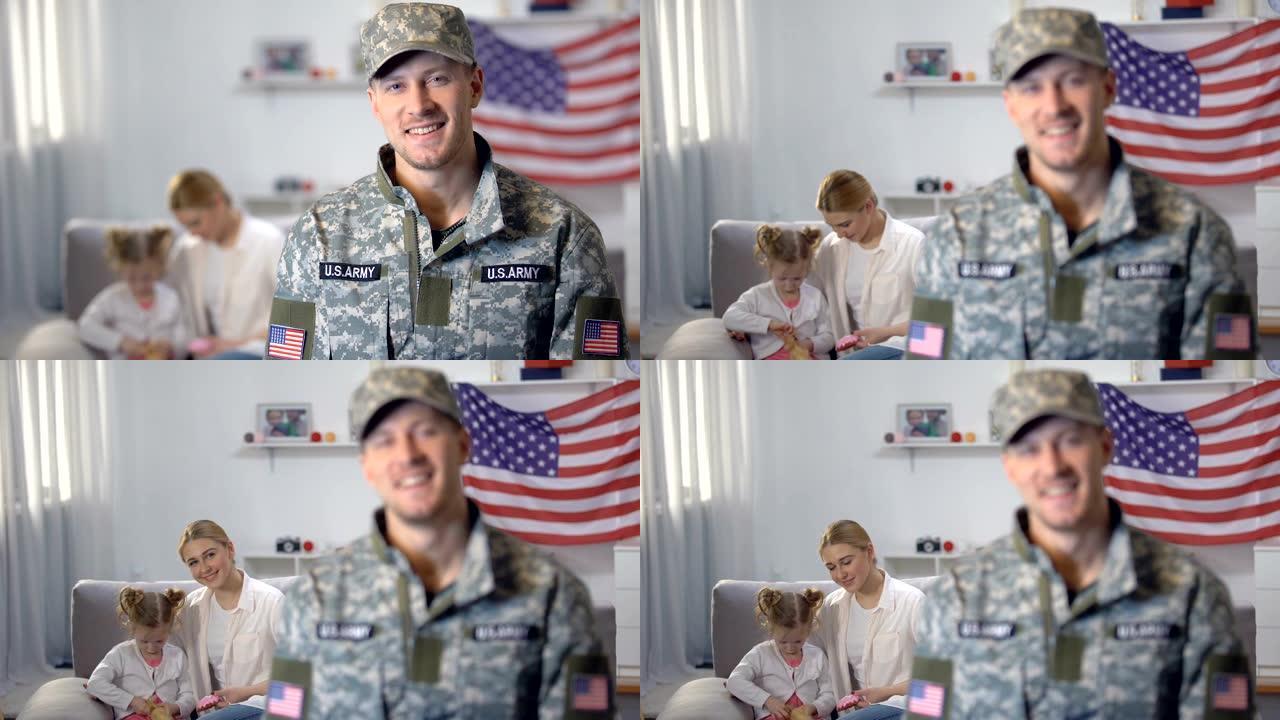 快乐的美军士兵对着镜头微笑，妻子和女儿坐在沙发上
