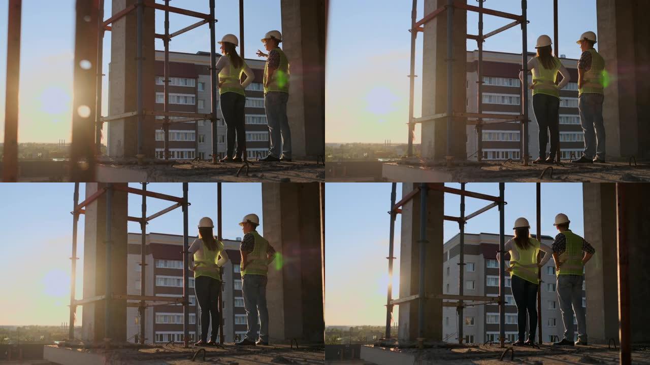 两名总工程师手里拿着图纸看着施工现场。从后面看。总工程师手里拿着蓝图看施工。