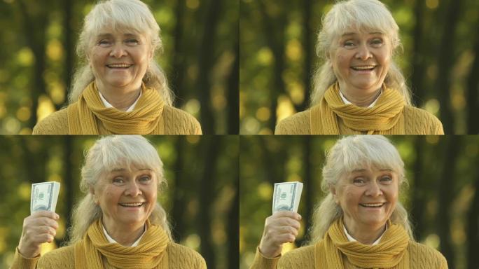 兴奋的老妇人向相机展示了一大笔钱，养老金补充，特写镜头