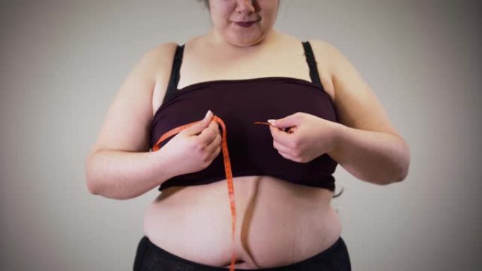 开朗的胖高加索女孩用卷尺测量胸部。穿着内衣的肥胖女性有超重问题。不健康的生活方式，肥胖。