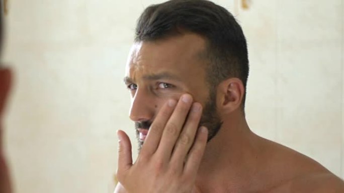 不快乐的男人在浴室的镜子前检查脸上的皱纹，老化