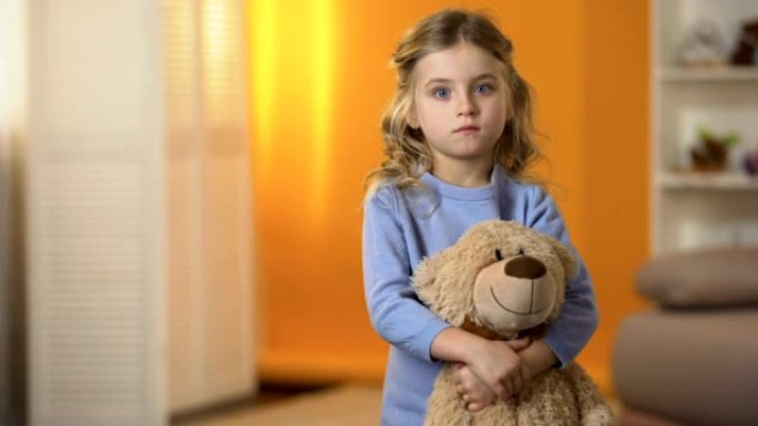 可爱的悲伤小女孩拥抱最喜欢的泰迪熊在孤儿院感到孤独
