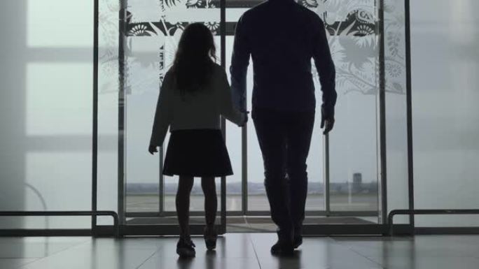 高加索男人和女孩从玻璃门走出机场的轮廓。家人去跑道。等待飞机起飞的年轻父女。一起旅行，旅游。