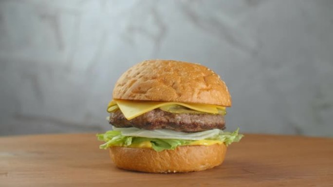 汉堡在木板上旋转。一个汉堡配肉排沙拉奶酪和西红柿，靠在灰色的墙上。