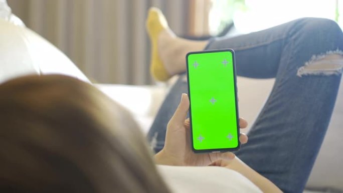 女人在沙发上使用带有绿屏的智能手机