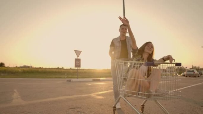 一个年轻的女性和男性在户外购物手推车上玩得开心的侧视图。多种族的年轻人在购物车上比赛。在停车区和他们