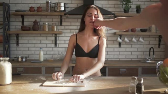 年轻性感的裸女在厨房做饭。男性用手去除女性嘴唇上的面粉污渍。缓慢的运动。