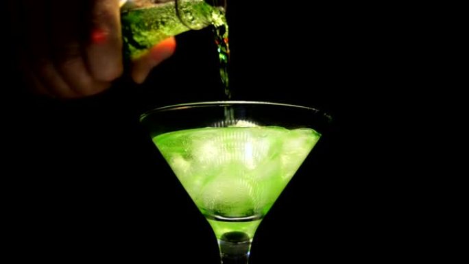 一名男子将绿色酒精饮料从瓶中倒入玻璃酒杯中