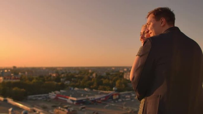 可爱的甜蜜幸福夫妇坐在屋顶上，城市城镇的日落美景令人惊叹。他们彼此相爱拥抱非常温柔太阳在头发之间。